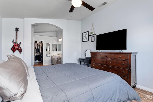 bedroom featuring arched walkways, connected bathroom, wood finished floors, visible vents, and baseboards