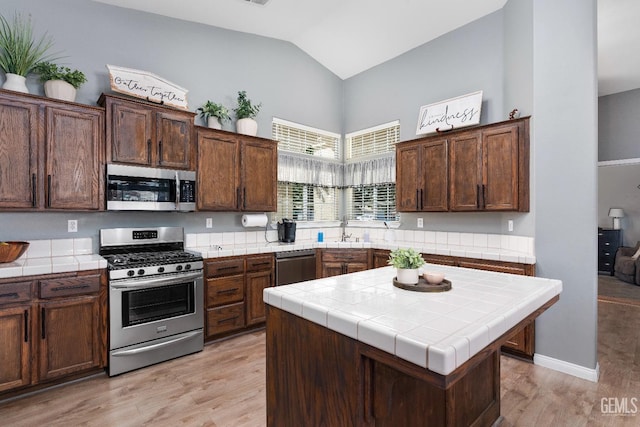 kitchen with stainless steel appliances, tile counters, lofted ceiling, a sink, and light wood-type flooring