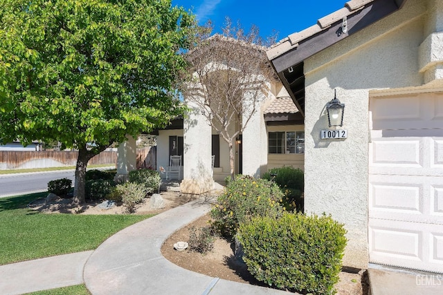 entrance to property with a garage, fence, and stucco siding