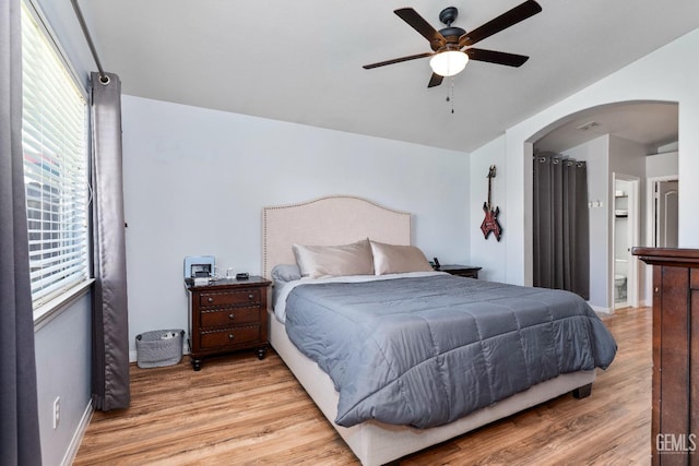 bedroom featuring arched walkways, baseboards, multiple windows, and light wood finished floors