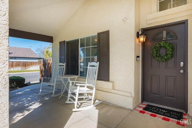 view of exterior entry with covered porch, fence, and stucco siding