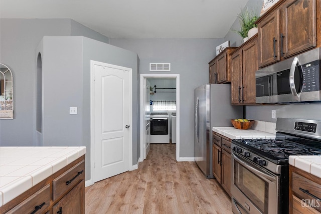 kitchen featuring tile countertops, washing machine and dryer, visible vents, appliances with stainless steel finishes, and light wood finished floors