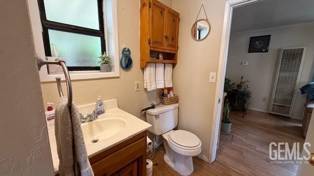 bathroom with a heating unit, wood finished floors, toilet, vanity, and baseboards