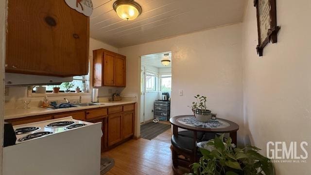 kitchen with brown cabinetry, white electric range, light wood-style flooring, light countertops, and a sink
