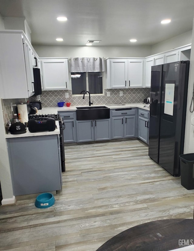 kitchen with white cabinets, sink, black refrigerator with ice dispenser, and gray cabinetry