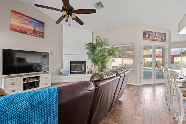 living room with ceiling fan, vaulted ceiling, a brick fireplace, and french doors