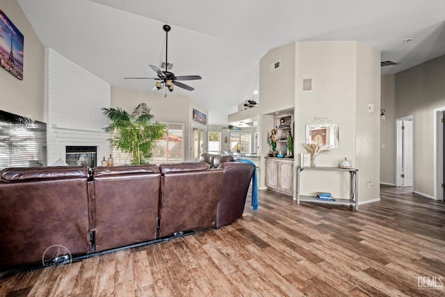 living room with ceiling fan, wood-type flooring, high vaulted ceiling, and a brick fireplace