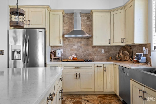 kitchen with pendant lighting, wall chimney exhaust hood, cream cabinetry, tasteful backsplash, and stainless steel appliances