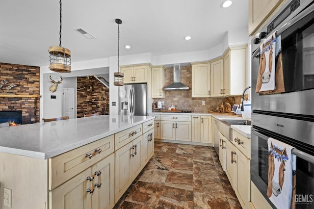 kitchen with pendant lighting, appliances with stainless steel finishes, wall chimney exhaust hood, a kitchen island, and tasteful backsplash