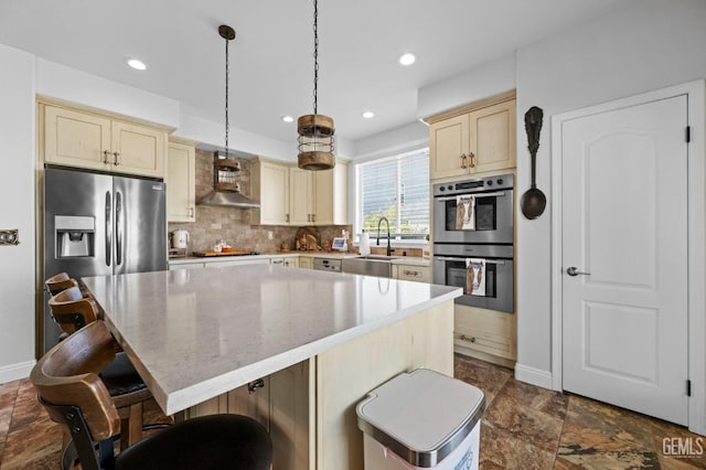 kitchen with hanging light fixtures, appliances with stainless steel finishes, sink, a center island, and wall chimney range hood