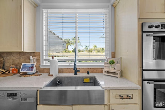 kitchen with cream cabinets, black dishwasher, sink, backsplash, and double oven