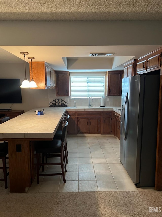 kitchen with sink, stainless steel refrigerator with ice dispenser, a kitchen bar, decorative light fixtures, and kitchen peninsula