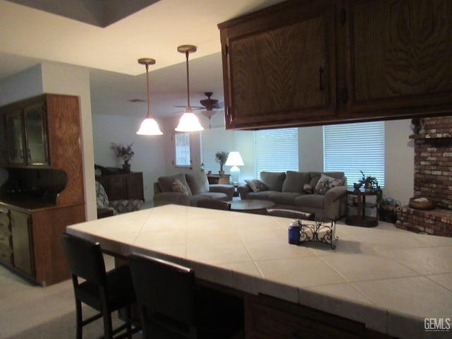 kitchen featuring dark brown cabinetry, a breakfast bar, tile counters, kitchen peninsula, and pendant lighting