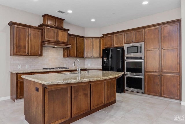 kitchen with appliances with stainless steel finishes, an island with sink, sink, backsplash, and light stone counters