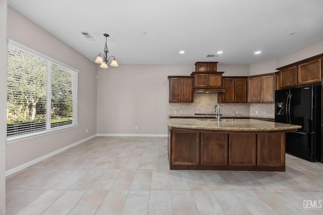 kitchen with light stone countertops, hanging light fixtures, backsplash, black fridge, and a chandelier