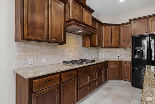 kitchen with stainless steel gas stovetop, black fridge, decorative backsplash, light stone countertops, and light tile patterned floors