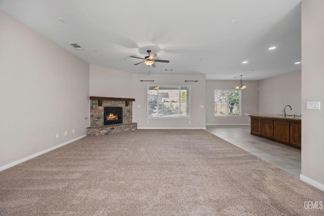 unfurnished living room with light colored carpet, a fireplace, sink, and ceiling fan with notable chandelier