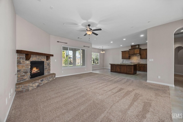 unfurnished living room featuring light carpet, ceiling fan, a fireplace, and sink