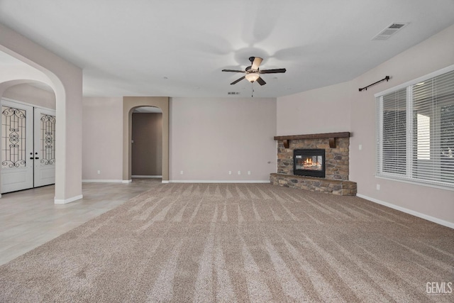 unfurnished living room with light carpet, ceiling fan, french doors, and a stone fireplace