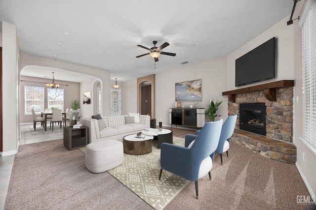 tiled living room with ceiling fan with notable chandelier and a stone fireplace