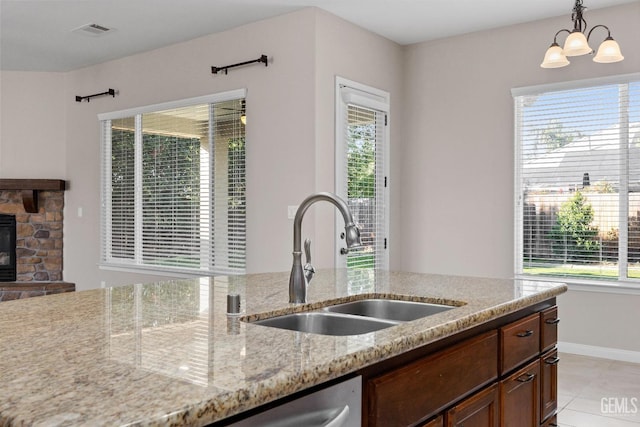 kitchen featuring a stone fireplace, plenty of natural light, hanging light fixtures, and sink