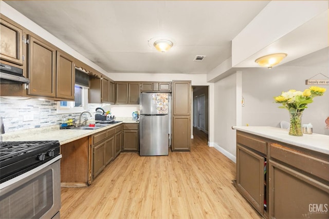 kitchen featuring light countertops, decorative backsplash, a sink, light wood finished floors, and appliances with stainless steel finishes