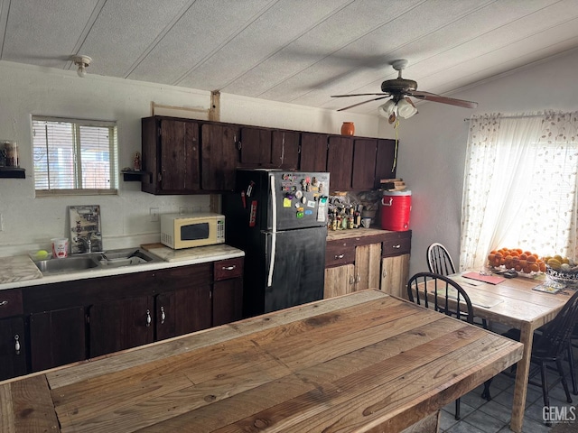 kitchen with freestanding refrigerator, light countertops, dark brown cabinetry, and white microwave