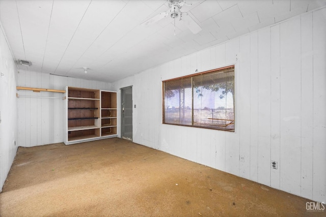 below grade area with wood walls, a ceiling fan, visible vents, and carpet floors