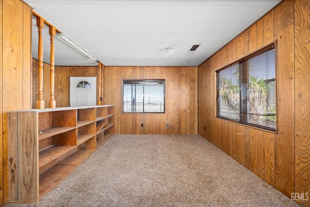 carpeted empty room featuring wood walls, visible vents, and a healthy amount of sunlight