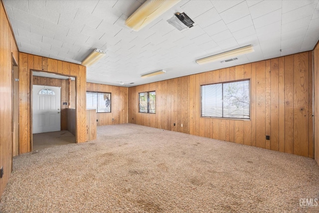 empty room featuring wood walls, carpet flooring, and visible vents