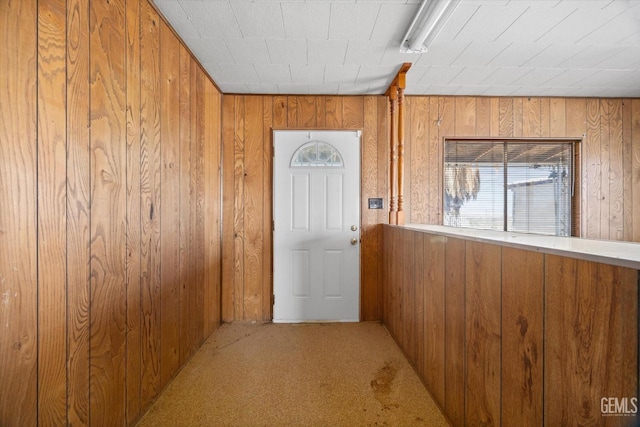 doorway to outside with wooden walls and carpet flooring
