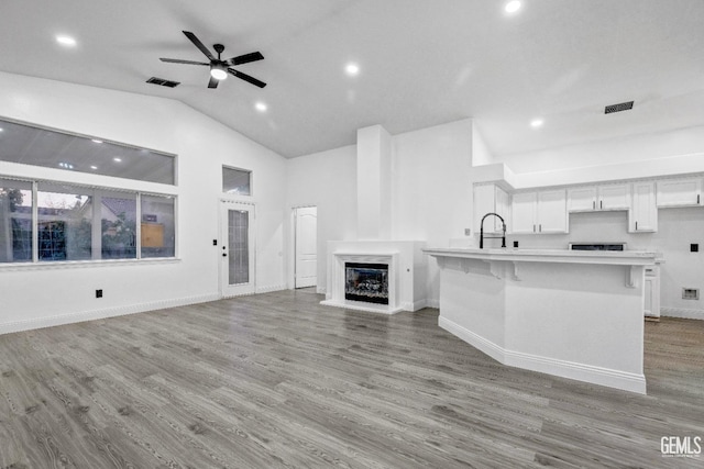 kitchen with a kitchen bar, sink, white cabinetry, an island with sink, and light hardwood / wood-style floors