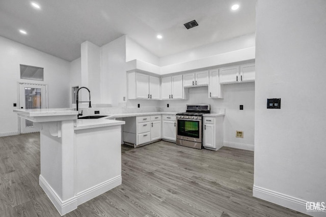 kitchen with sink, white cabinets, kitchen peninsula, stainless steel gas range oven, and light wood-type flooring