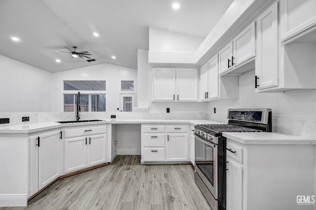 kitchen featuring white cabinetry, gas range, lofted ceiling, and sink