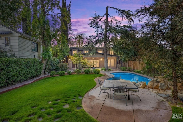 pool at dusk featuring a patio area and a lawn