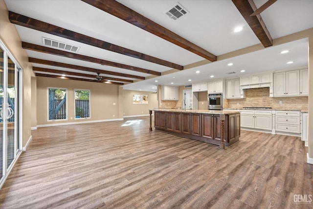 kitchen with stainless steel gas stovetop, white cabinetry, backsplash, a large island with sink, and light stone counters