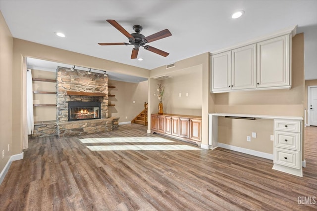 unfurnished living room with ceiling fan, a fireplace, built in desk, and hardwood / wood-style floors