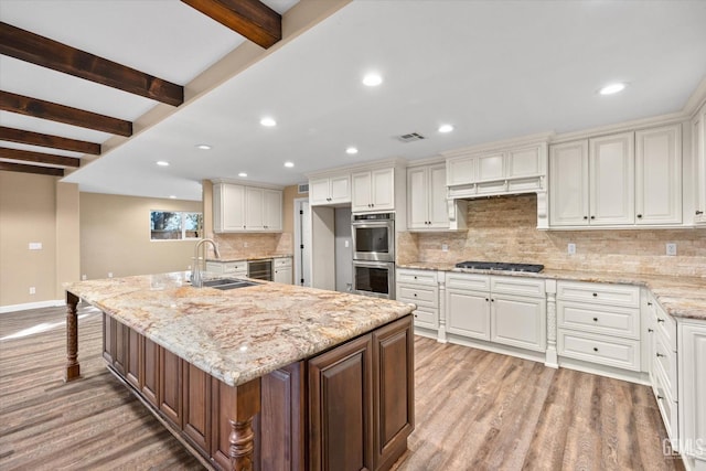 kitchen with a large island, sink, double oven, light stone countertops, and white cabinets