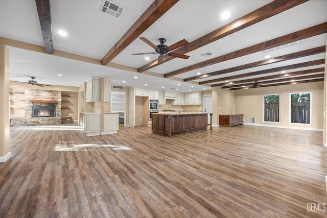 unfurnished living room featuring wood-type flooring, a fireplace, beamed ceiling, and ceiling fan