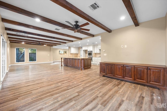 unfurnished living room featuring beamed ceiling, ceiling fan, and light hardwood / wood-style floors