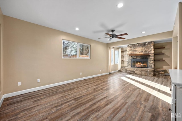 unfurnished living room with dark wood-type flooring, ceiling fan, and a stone fireplace