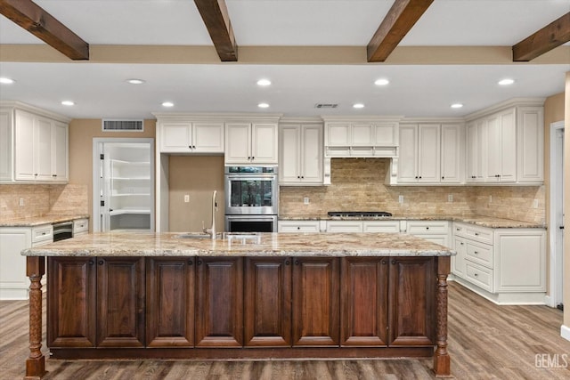 kitchen featuring a kitchen island with sink, light stone countertops, beam ceiling, and stainless steel appliances