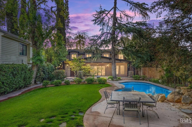 pool at dusk featuring a patio and a yard