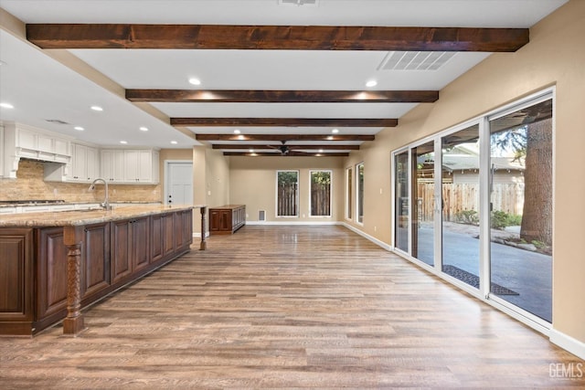 kitchen featuring tasteful backsplash, white cabinetry, light stone countertops, light wood-type flooring, and a spacious island