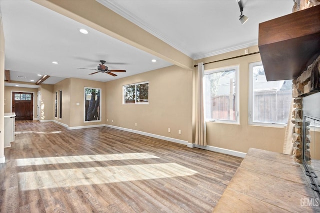 unfurnished living room with a stone fireplace, a wealth of natural light, ornamental molding, and light wood-type flooring