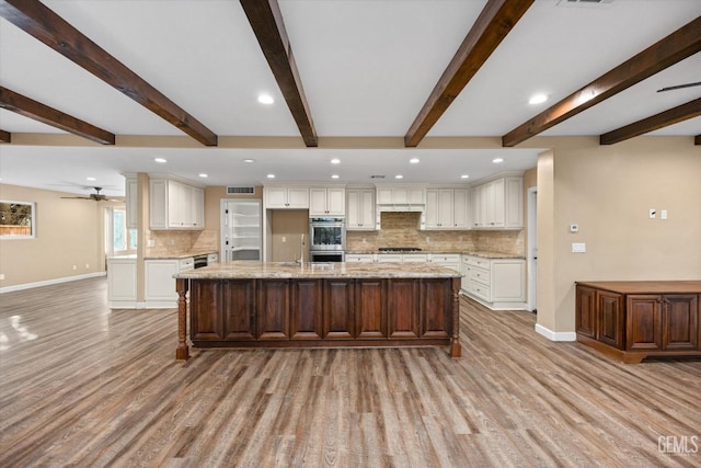 kitchen with appliances with stainless steel finishes, white cabinets, light hardwood / wood-style floors, light stone countertops, and a spacious island