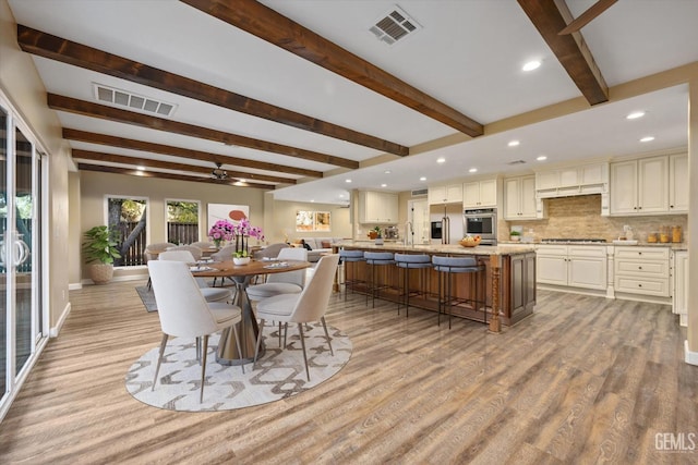 dining area with sink, ceiling fan, beamed ceiling, and light wood-type flooring