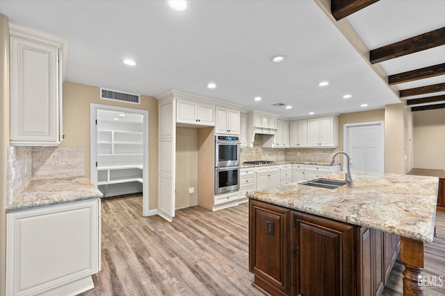 kitchen with light stone counters, white cabinetry, stainless steel appliances, and sink