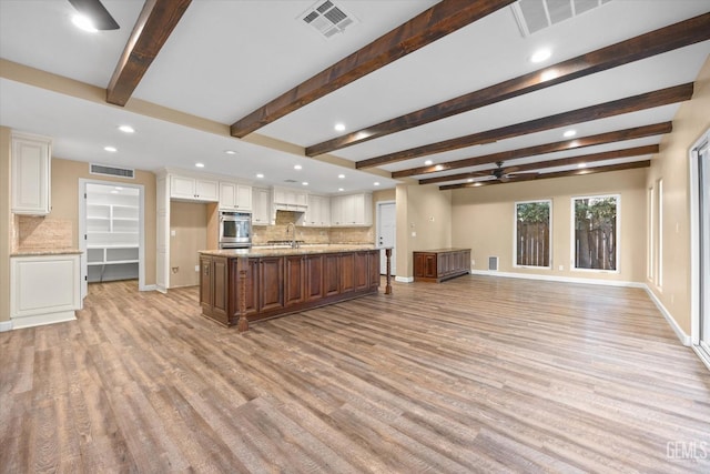 kitchen featuring white cabinetry, a large island, sink, and light stone counters