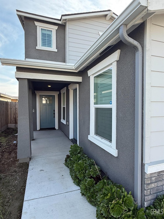 view of exterior entry featuring fence and stucco siding